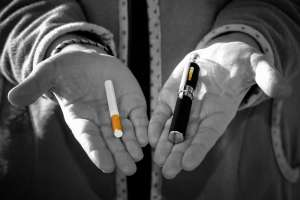 A person holding two cigarettes, one in each hand, against a neutral background.