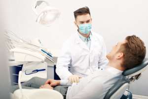  A man seated in a dental chair, wearing a mask, preparing for a dental procedure