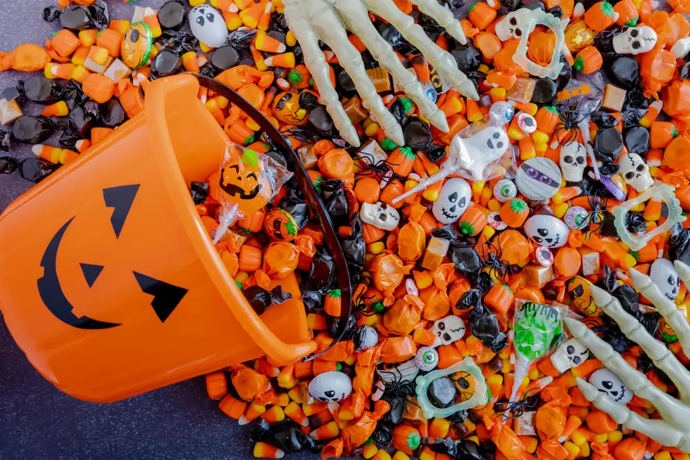 A bucket filled with Halloween candy, featuring a skeleton hand and a carved pumpkin beside it.