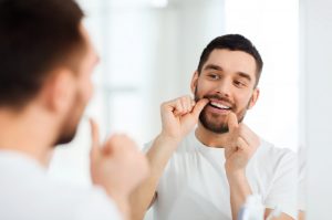 A man brushes his teeth while standing in front of a mirror, focusing on his dental hygiene routine.