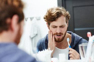 A man brushes his teeth while standing in front of a mirror, focusing on his dental hygiene routine.