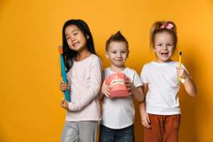Three smiling children holding toothbrushes, promoting dental hygiene and healthy habits.
