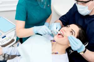 A patient receiving dental treatment from two professionals wearing gloves and masks