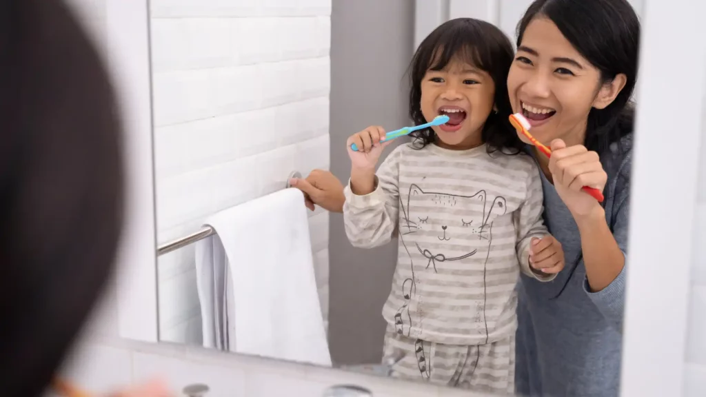 A mother and child brushing their teeth together in the bathroom