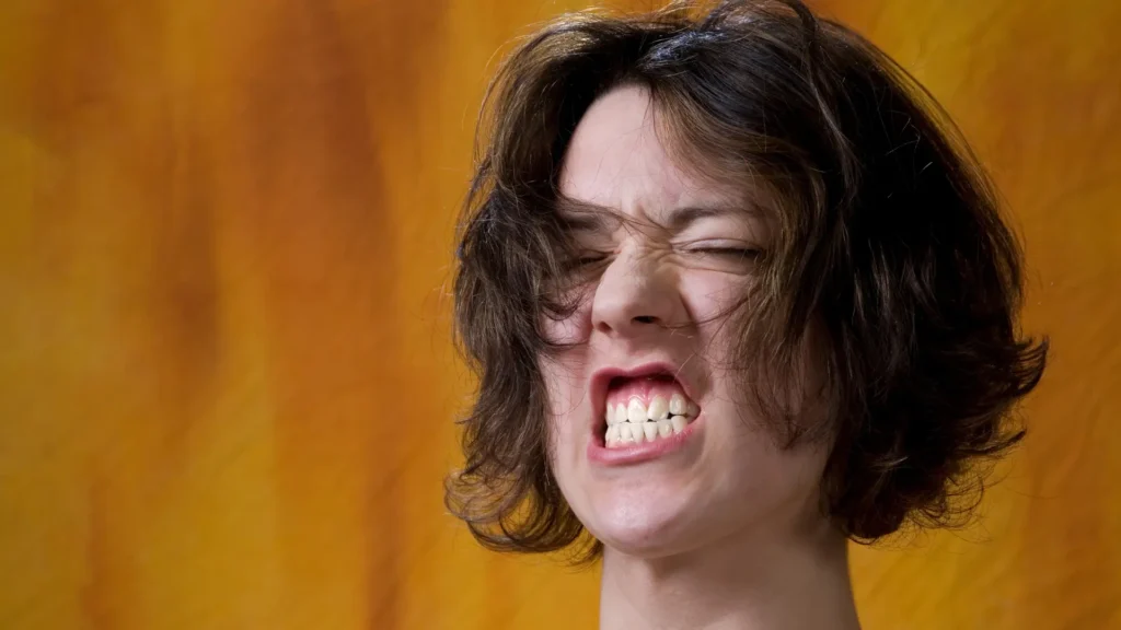 Close-up of a woman grimacing in pain or frustration, showing clenched teeth