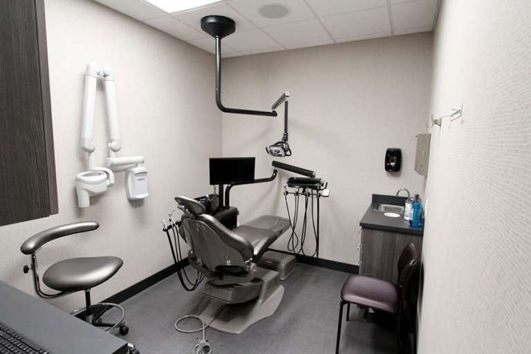 A modern dental examination room featuring a dental chair, overhead light, monitor, and various dental equipment