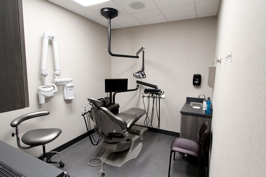 A modern dental examination room featuring a dental chair, overhead light, monitor, and various dental equipment
