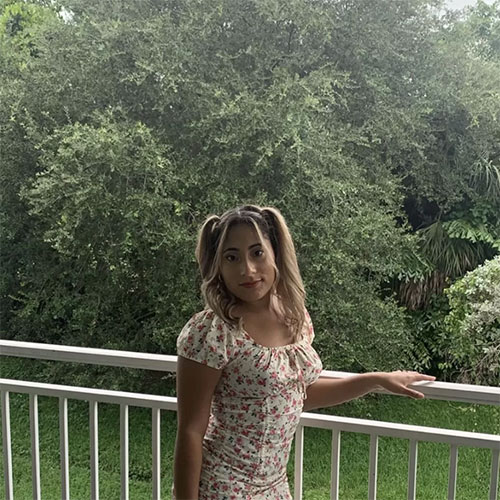 A woman in a floral dress stands gracefully on a balcony, enjoying the view.