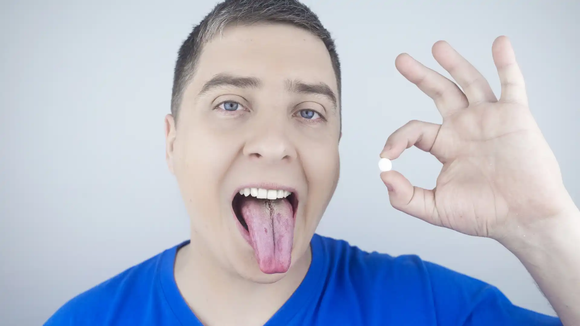 Man sticking out tongue while holding a small pill