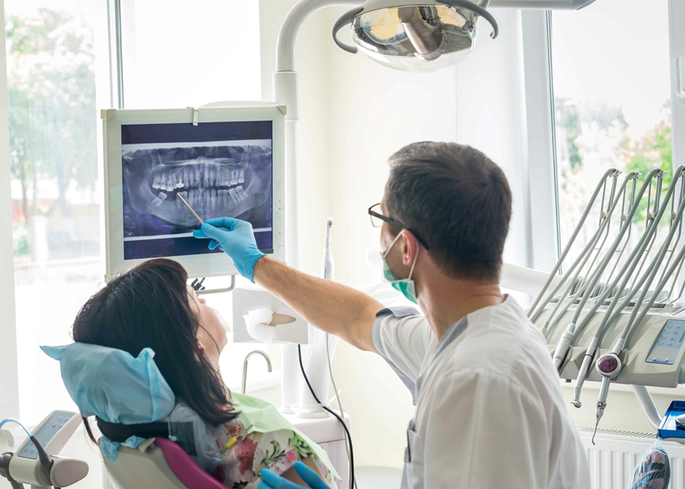 Dentist wearing a mask and gloves showing a dental X-ray to a patient in a clinic.