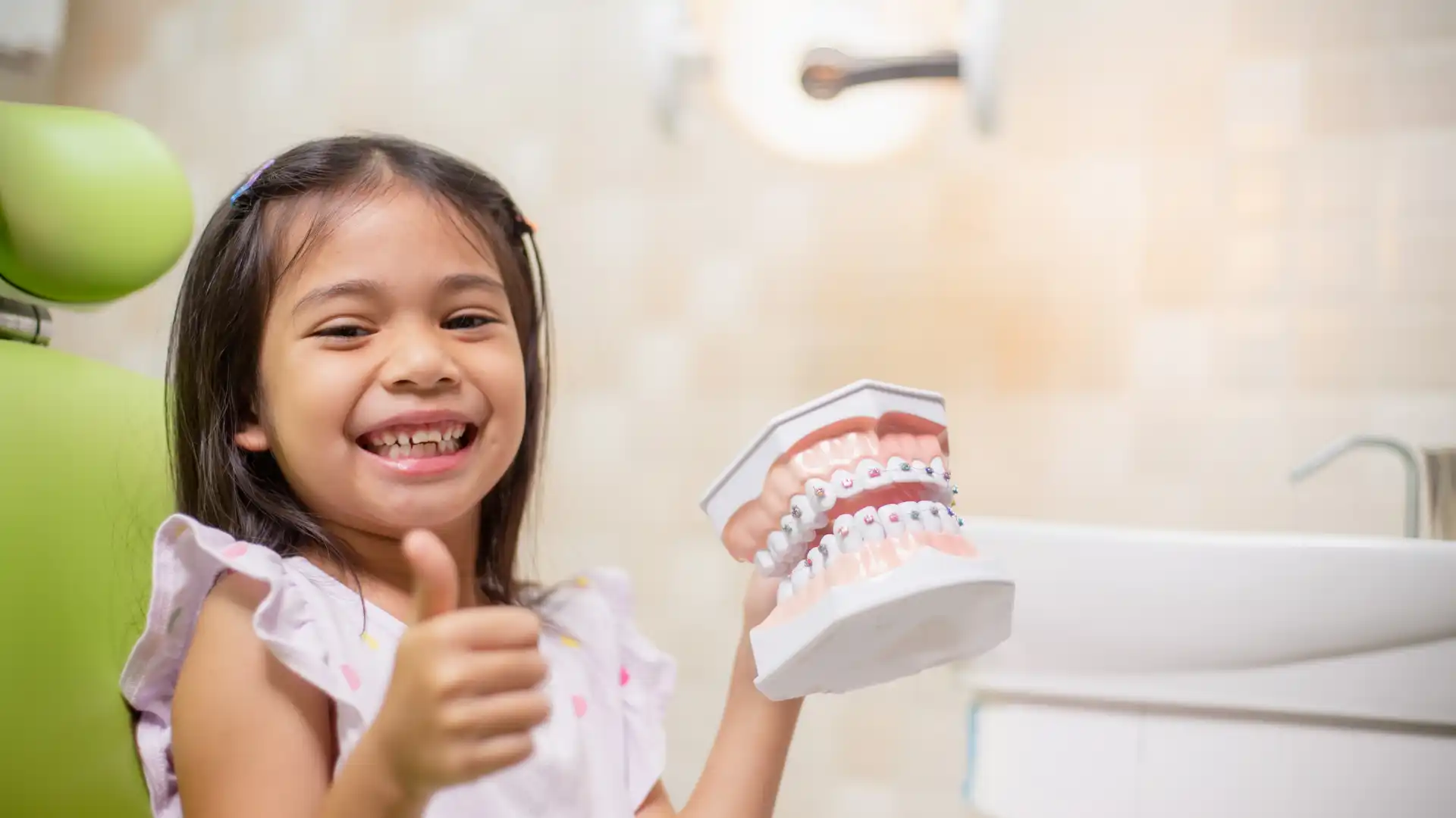 Happy young girl holding a dental model, giving a thumbs-up for good oral health.