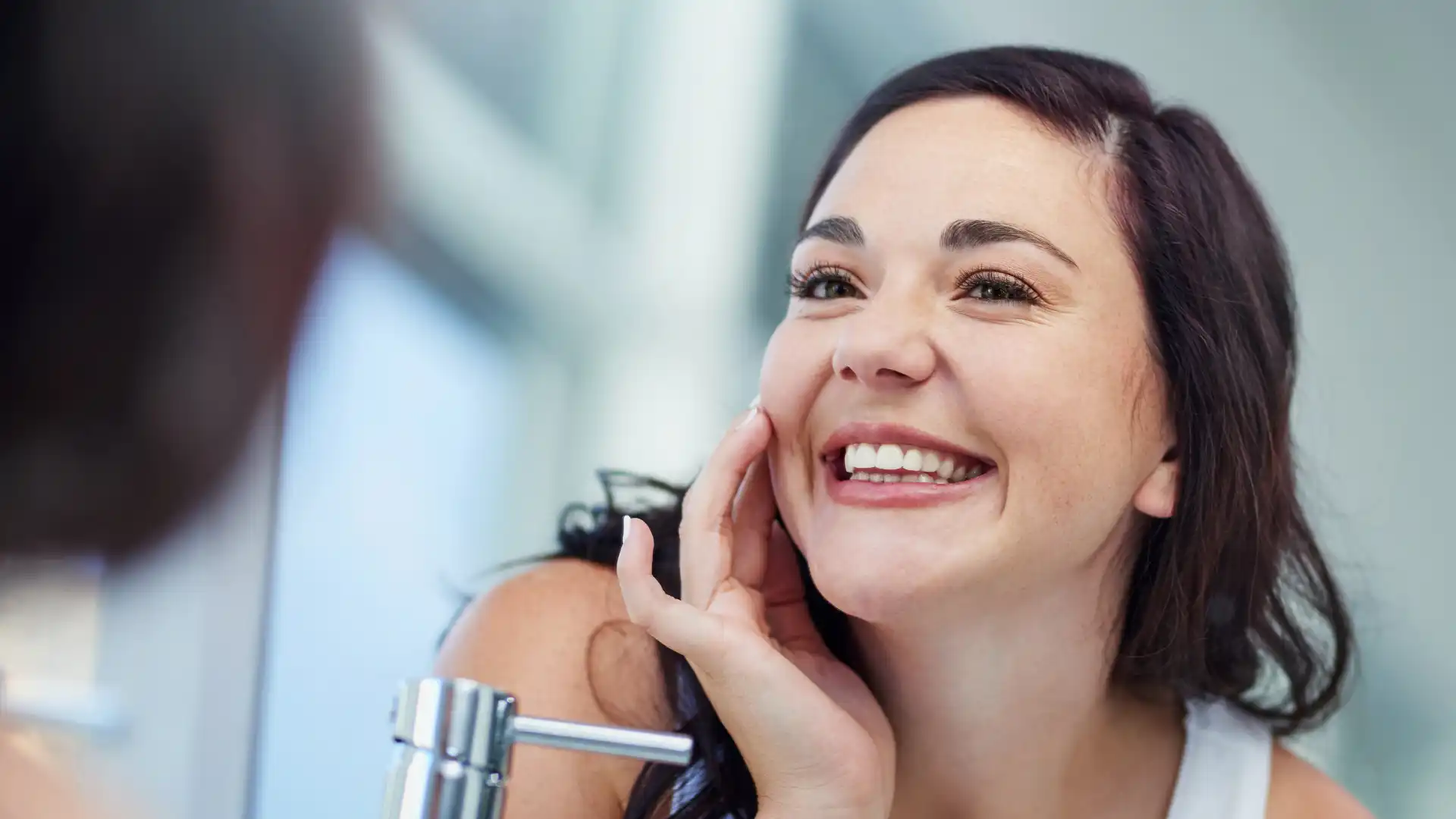 Smiling woman looking at her reflection in the mirror with bright, healthy teeth