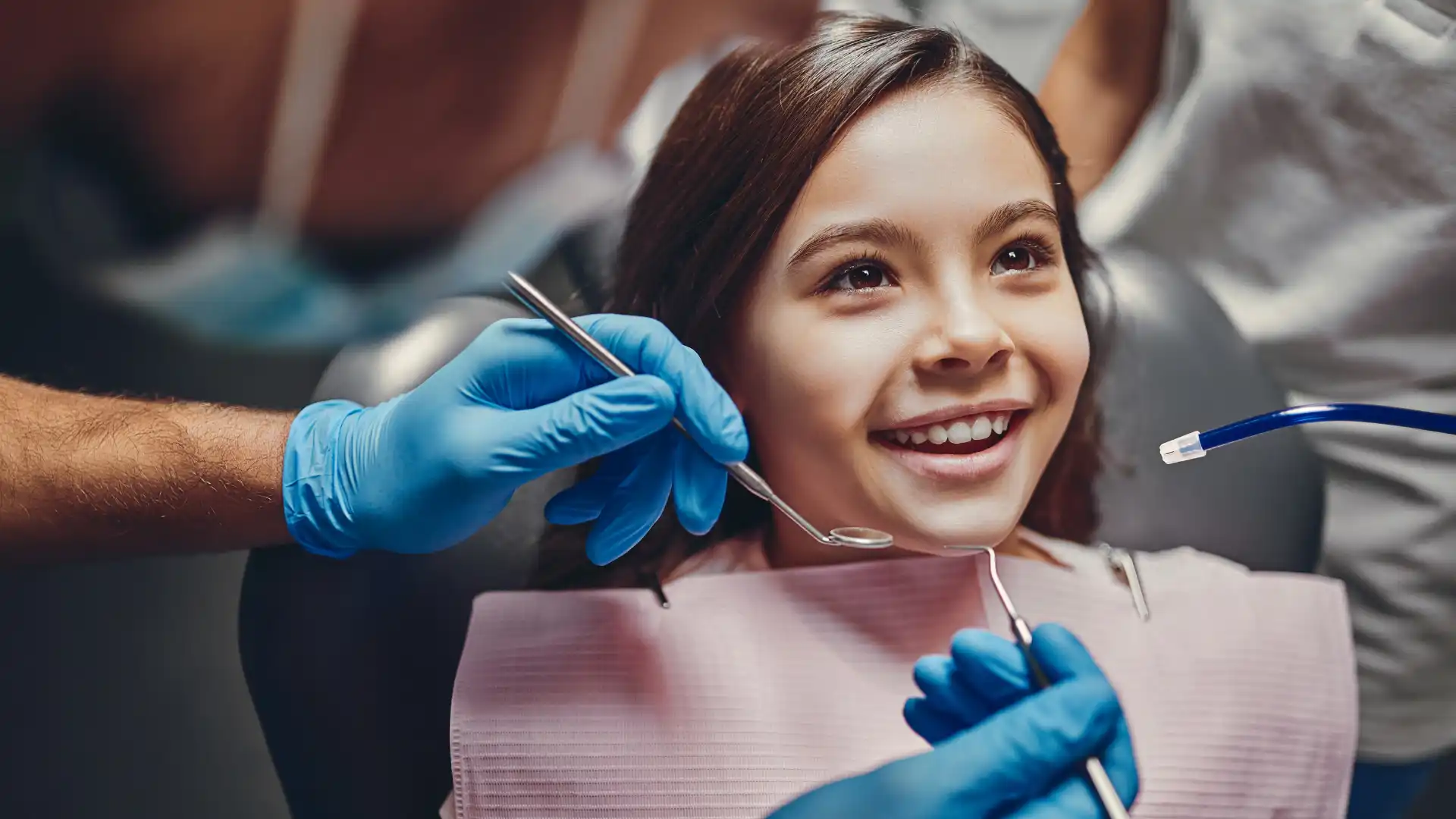 Smiling young girl receiving a dental check-up from a professional wearing blue gloves.