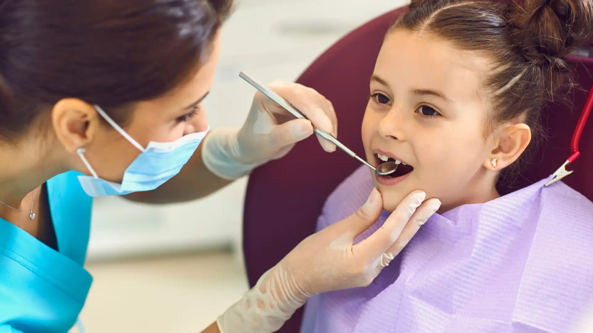 Young girl receiving a dental check-up from a dentist wearing gloves and a mask.