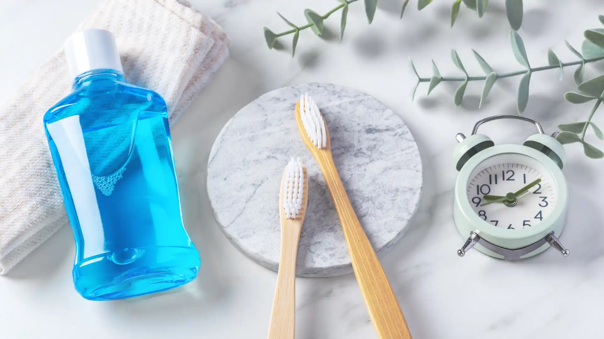 Bamboo toothbrushes with mouthwash and natural decor on a marble surface.