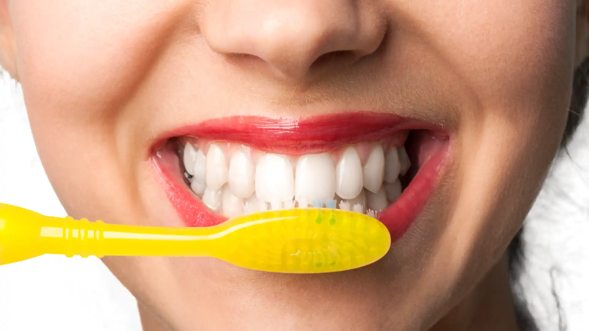 Smiling woman brushing teeth with a yellow toothbrush