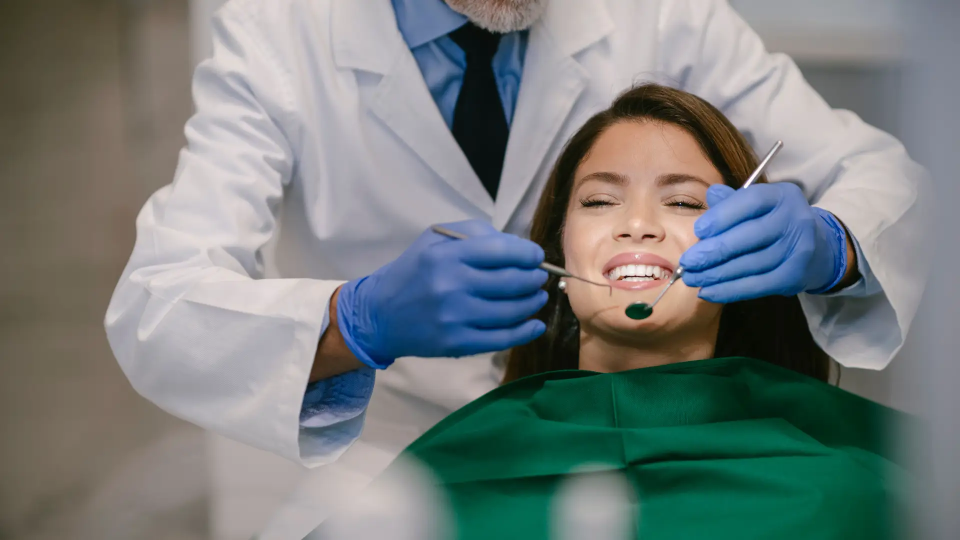 Dentist in gloves examining a female patient's teeth as she winces slightly