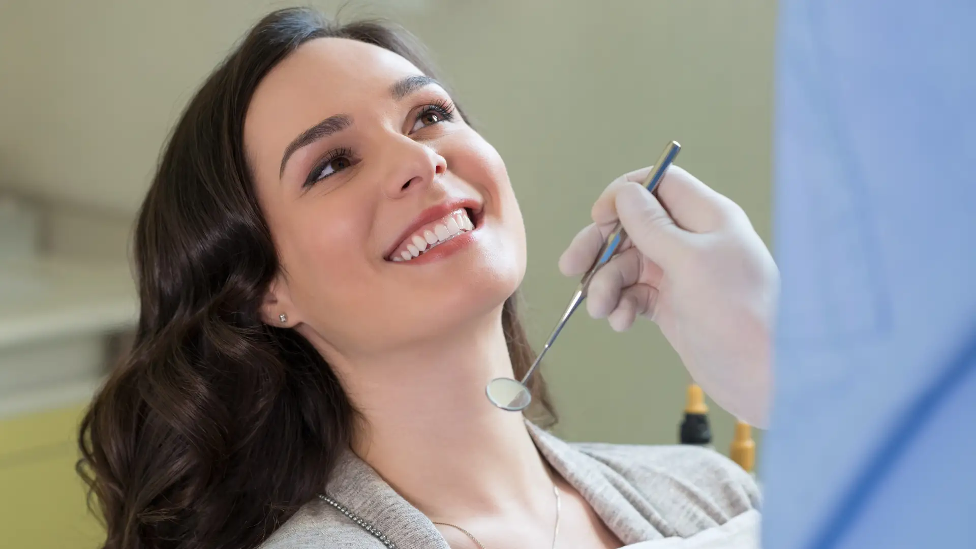 Smiling woman receiving a dental check-up from a gloved dentist using a mirror tool.