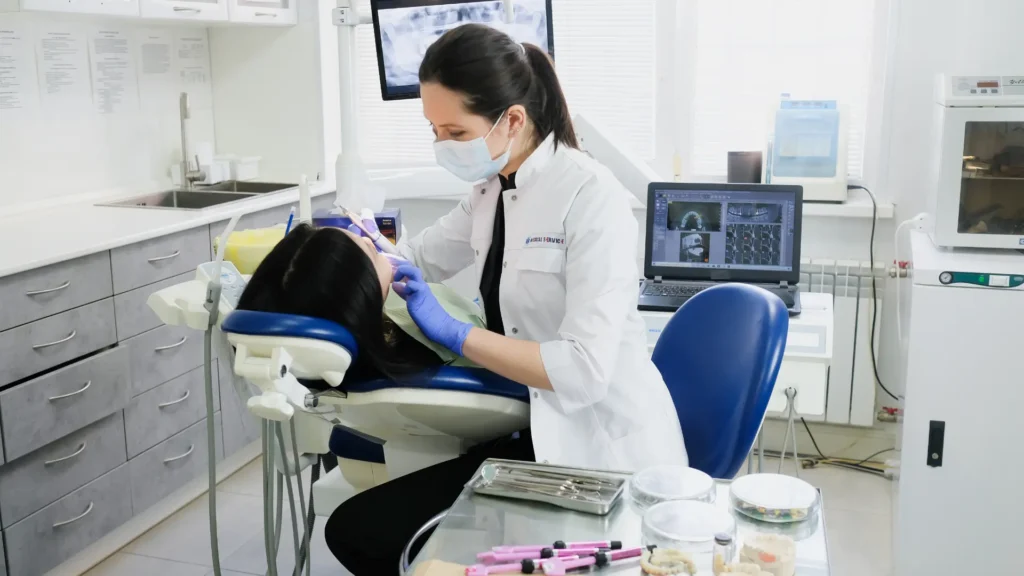 A dentist in a white coat and protective gear performing a dental procedure on a patient in a dental chair.