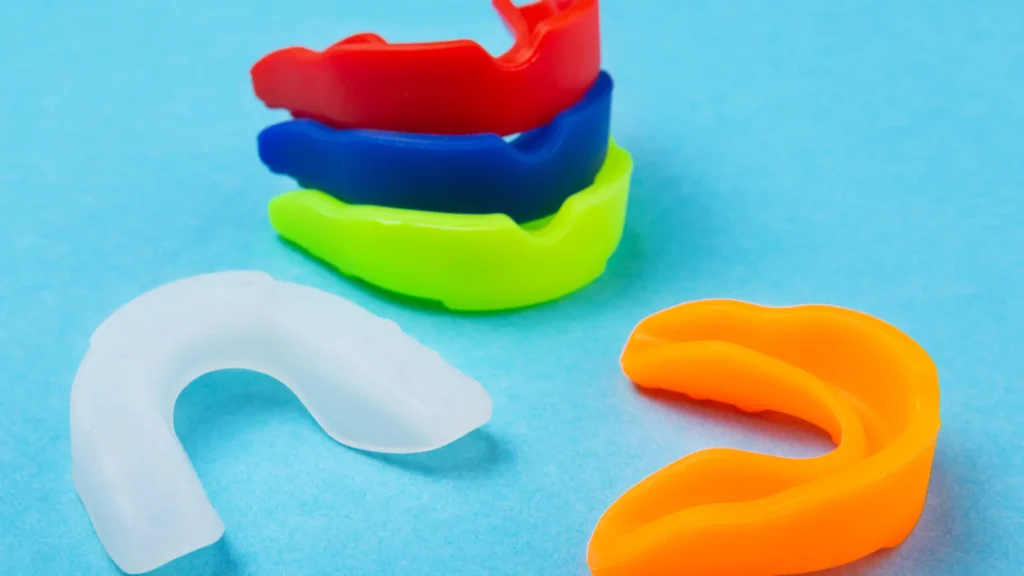 A collection of colorful mouthguards in red, blue, green, orange, and white stacked on a blue background.