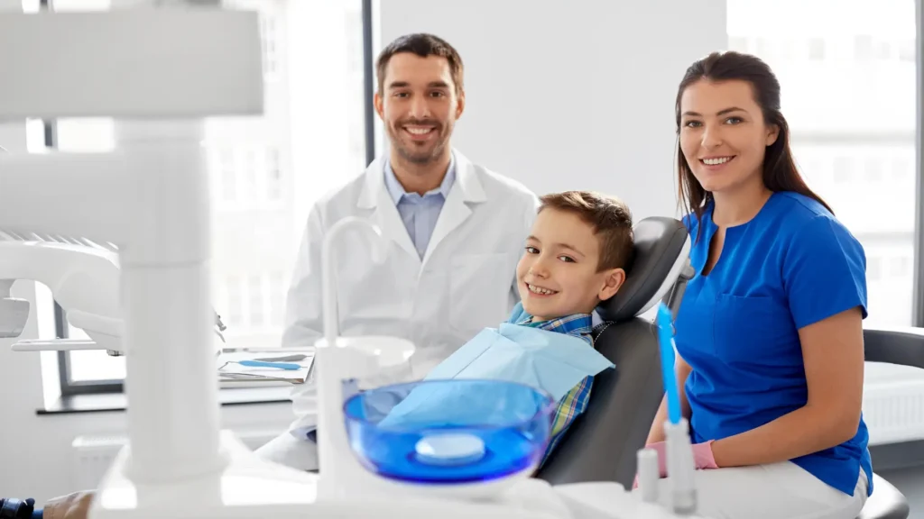 Young boy sitting in a dental chair with a dentist and assistant smiling beside him.