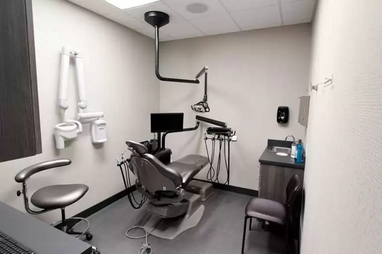 A modern dental examination room featuring a dental chair, overhead light, monitor, and various dental equipment