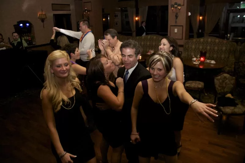A group of people dressed in formal attire, socializing and dancing in a dimly lit venue with a cozy atmosphere.