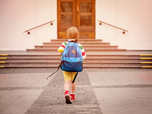 A young girl with a backpack strolls down a street, embodying innocence and adventure.