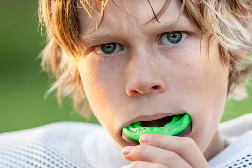 A young boy smiles while holding a green toothbrush in his hand, ready for his dental care routine.