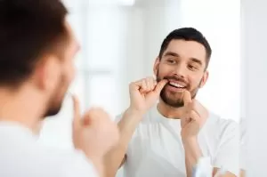 A man brushes his teeth while standing in front of a mirror, focusing on his dental hygiene routine.