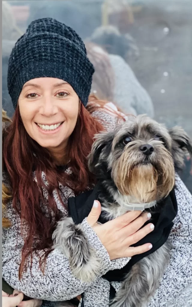 A smiling woman in a beanie holding a small, scruffy dog.
